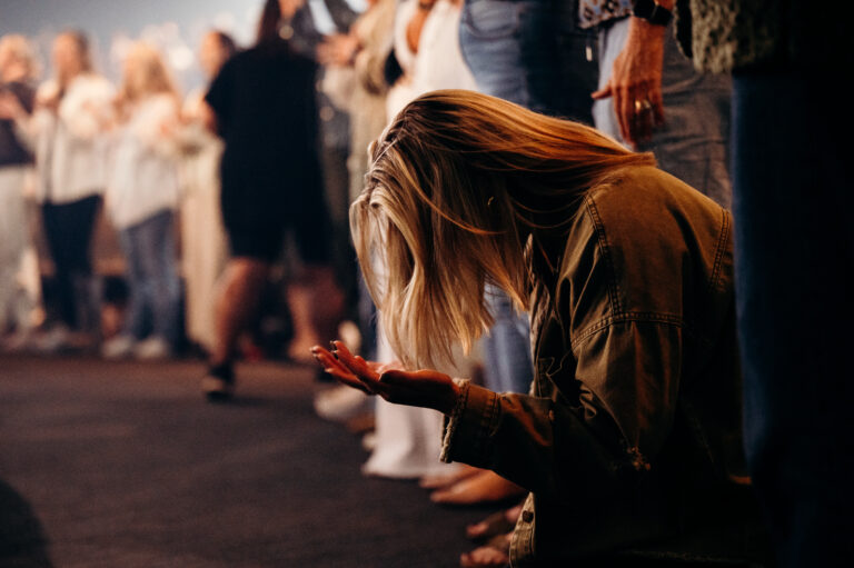 A women is kneeling on the ground with her hands outstretched and head bowed in a group of worshippers