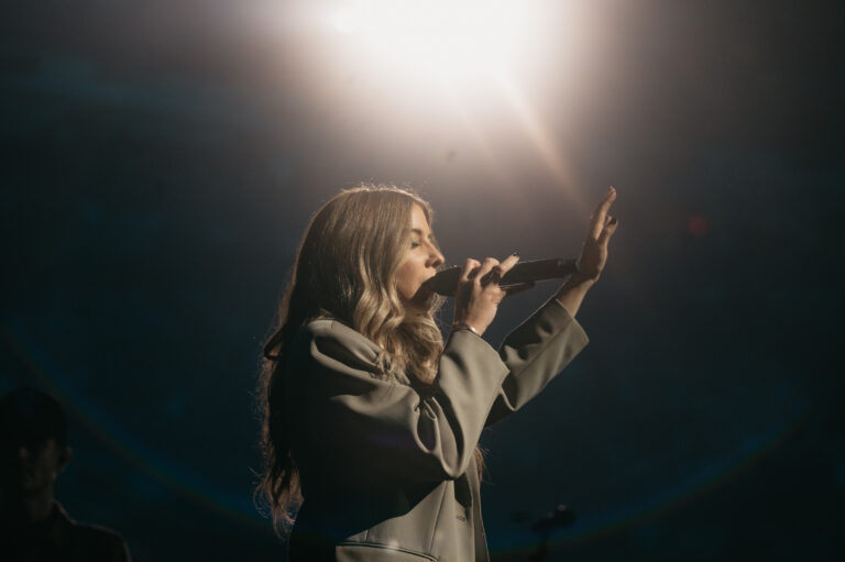 A woman leads worship holding a mic and with hand outstretched in worship