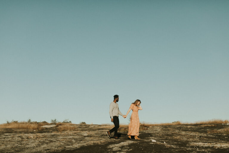 A man and women walk in an empty rocky field, holding hands